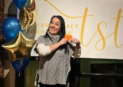 TST member at Foundation event, smiling and holding an orange envelope.